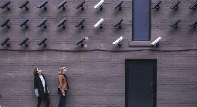 personer mot vägg fylld med säkerhetskameror.