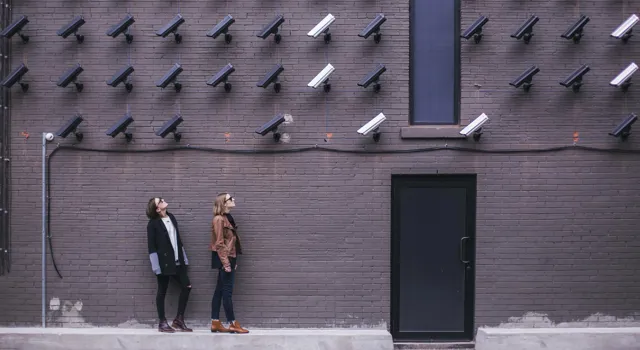 personer mot vägg fylld med säkerhetskameror.